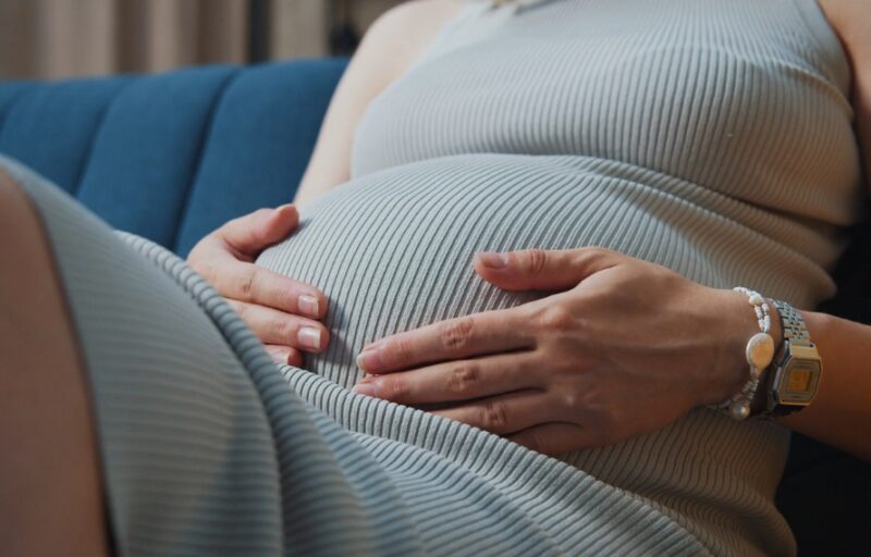Trudnica sedi i drži ruke na stomaku, opuštajući se pre spavanja i ublažavajući nelagodnost u trudnoći.